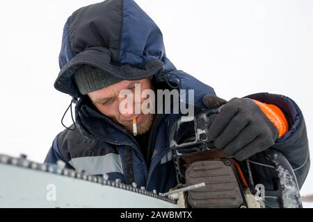 A worker in a blue jacket sharpens a chainsaw chain. Stock Photo