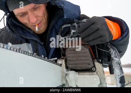 A worker in a blue jacket sharpens a chainsaw chain. Stock Photo
