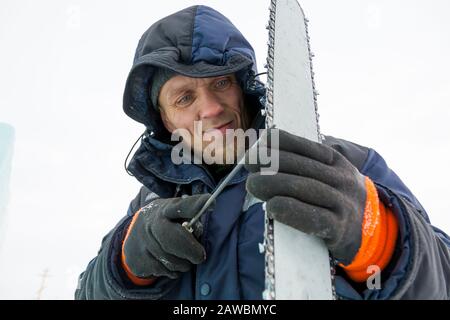 A worker in a blue jacket sharpens a chainsaw chain. Stock Photo