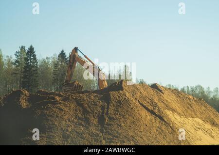 Excavator stands on the sand hill and digs the ground. part of construction earthmoving equipment. digging and filling the soil with an excavator buck Stock Photo