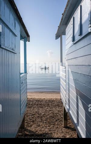 Blue boat viewed through the beach huts on Thorpe Bay beach, Essex, England, on a still day Stock Photo