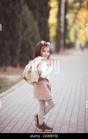 Cute kid girl 3-4 year old wearing trendy clothes posing in cityoutdoors.  Looking at camera. Childhood. Autumn season. Stock Photo