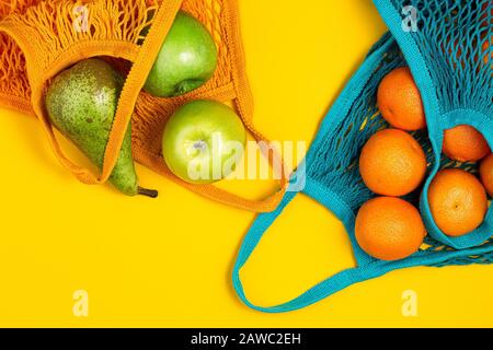 Tangerines and green apples in string bag on yellow background. Zero waste, plastic free concept. Healthy clean eating diet and detox. Summer fruits. Stock Photo