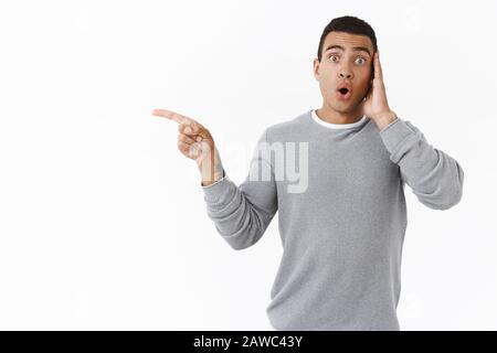 Oh my have you seen it. Amazed and curious, astonished young hispanic guy pointing left and folding lips from excitement and interest, found exellent Stock Photo
