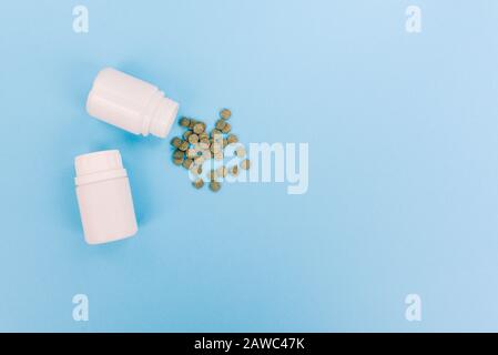 Green scattered tablets. White plastic jars with drugs, vitamins and antibiotics. Treatment of diseases with medicines Stock Photo