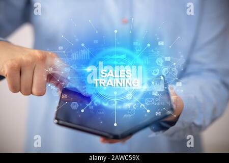 Businessman holding a foldable smartphone with SALES TRAINING inscription, new business concept