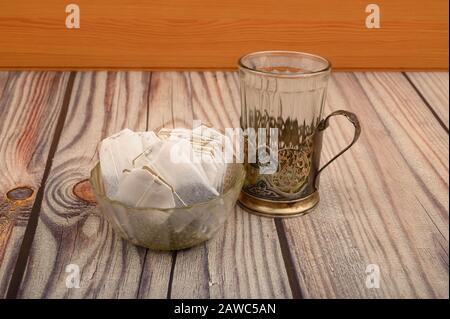Tea bags in a glass vase and an empty faceted glass in a vintage Cup holder on a wooden background. Close up Stock Photo