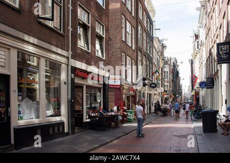 View of people walking on Warmoesstraat street in Amsterdam. It is one of the oldest streets with many cafes, restaurants and shops. It is a sunny sum Stock Photo