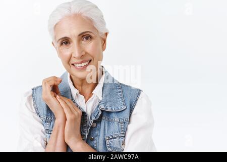 Close-up portrait pleasant, charming old modern lady, senior woman with grey hair in stylish denim vest, touching hands, apply daily anti-aging creme Stock Photo