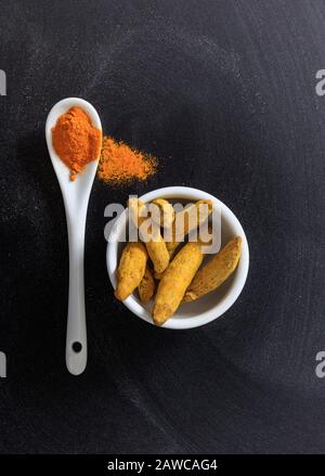 Turmeric curcumin or curcuma roots and powder in porcelain bowl and spoon, black background, top view Stock Photo