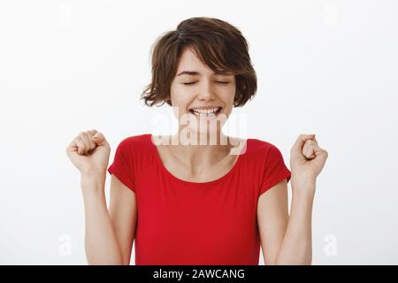 Yes accomplishment. Successful happy delighted lucky cute woman short curly haircut close eyes triumphing satisfied clench fists victory celebration Stock Photo