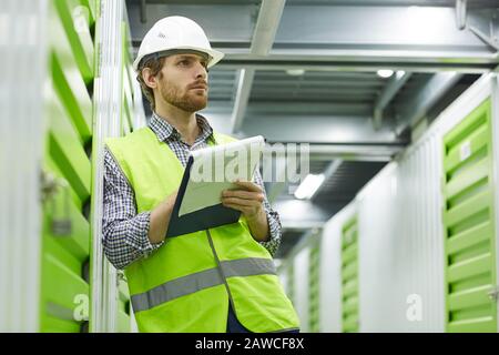 Serious young manual worker in working clothing standing and working with documents in warehouse Stock Photo