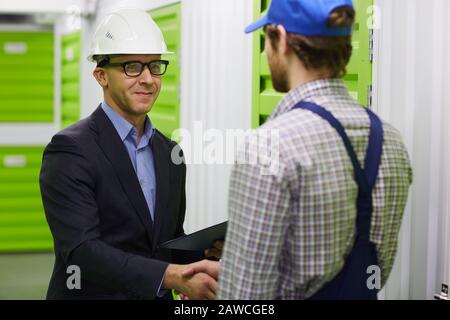 Confident businessman in suit and in work helmet shaking hand to manual worker and thanks him for his good job Stock Photo