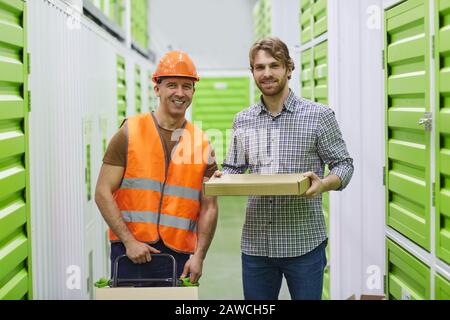 Portrait of two young workers with cardboard boxes smiling at camera while working in warehouse Stock Photo