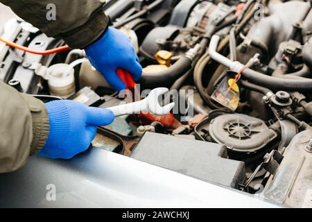 Car mechanic engineer using a wrench in process of fixing a car. Male hands of car mechanic with a wrench working in garage. Man in gloves working in Stock Photo