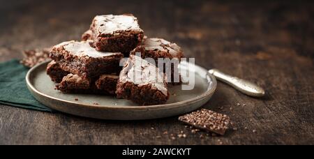 Slices Homemade brownie cakes with dark chocolate sprinkled with icing sugar on a dark background. Place for text. Banner Concept Stock Photo
