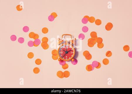 Vintage alarm clock shows 10 hours and 10 minutes among the multicolored confetti as concept for celebrating top view festive background Stock Photo