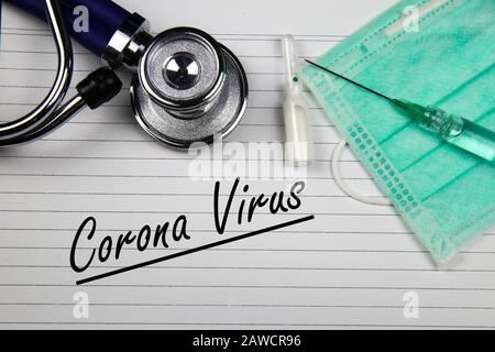 View on white index card with stethoscope, vial, syringe, green surgical face mask with words corona virus Stock Photo