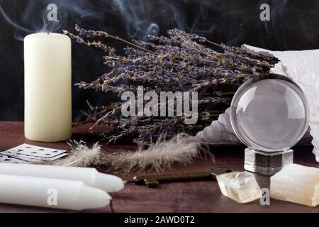 Divination with white candles, lavender, fortune-telling ball, stones. Halloween background, occult and esoteric objects on witch wooden table Stock Photo