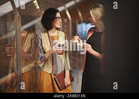 Two successful colleagues smiling and talking to each other during coffee break at office Stock Photo