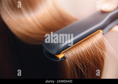 Professional equipment for hairdressers. Black hair iron in hand of master straightens with keratin Stock Photo