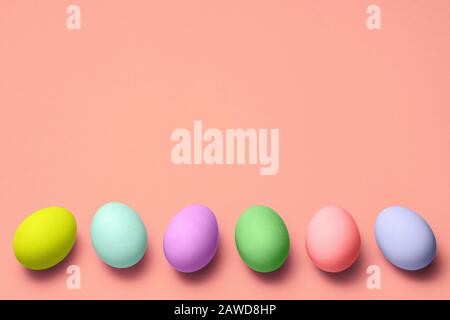 row of eggs of different colors on bottom on pink background with copyspace. happy easter Stock Photo