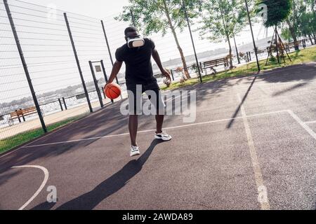 Outdoors Activity. African man in vr headset playing basketball on court watching video Stock Photo