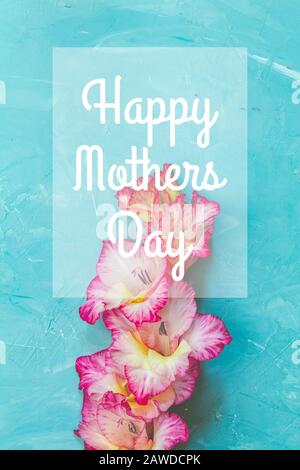 Happy Mothers Day phrase in the frame. Border frame made of pink gladiolus on blue concrete background. Pattern of gladiolus with space for your text, Stock Photo