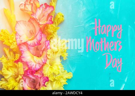 Happy Mothers Day phrase. Border frame made of yellow and pink gladiolus flowers on light blue background. Pattern of gladiolus with space for your te Stock Photo