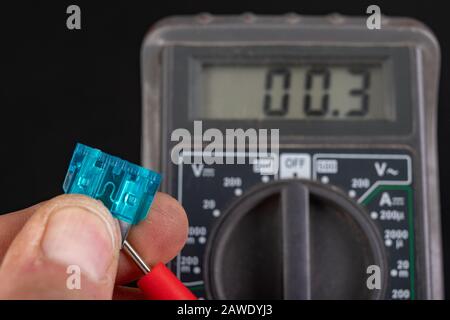 Measurement of resistance of car fuses with an electric meter. Checking the conductivity of electrical protections in the installation. Dark backgroun Stock Photo