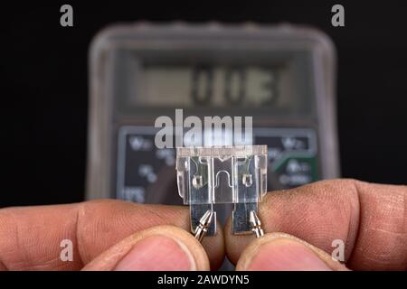 Measurement of resistance of car fuses with an electric meter. Checking the conductivity of electrical protections in the installation. Dark backgroun Stock Photo