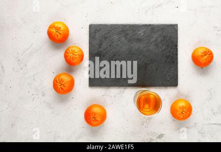 A cutting board made of gray slate is surrounded by orange fruits of mandarins randomly lying nearby on a gray concrete background, copy space. Stock Photo