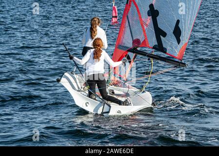 Two Girls Sailing small sailboat with long red hair viewed closeup from behind. Teamwork by junior sailors racing on saltwater Lake Macquarie. Stock Photo