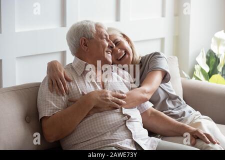 Happy elderly husband and wife relax hugging on couch Stock Photo