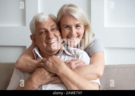 Loving senior husband and wife hugging looking at camera Stock Photo