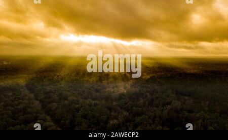 Sun rays shining dramatically through the clouds onto forest canopy. Stock Photo