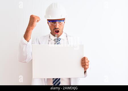 Young chemist man wearing security helmet holding signboard over isolated background annoyed and frustrated shouting with anger, crazy and yelling wit Stock Photo