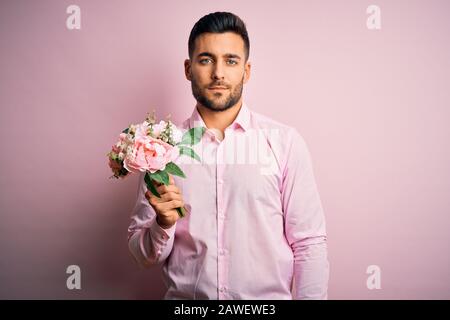 Young romatic man holding bouquet of spring flowers over pink isolatd ...