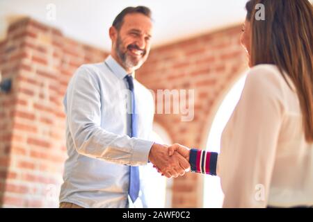 Two middle age business workers smiling happy and confident. Working together with smile on face doing handsake at the office Stock Photo