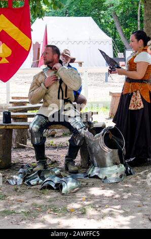 Holly Michigan, USA July 27 2014; a man removes hot heavy armor after a performance at a renaissance fair, as his partner fans him from the side Stock Photo