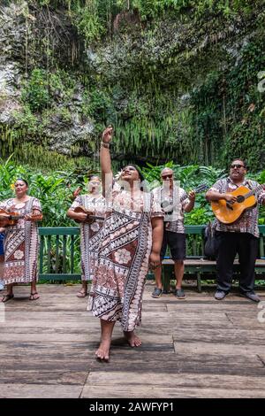 Kamokila Village, Kauai, Hawaii, USA. - January 16, 2020: Local folk band performs on stage in front of Fern Grotto. Female singer in front. Green bac Stock Photo