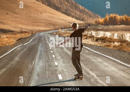 Lonely unrecognized skateboarder rides on longboard at straight mountain road Stock Photo