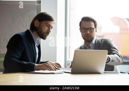 Two serious businessmen colleagues discussing project, looking at laptop screen Stock Photo