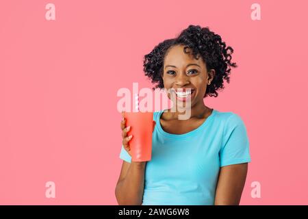 Close up portrait of a happy young smiling woman holding a drinking cup with straw and looking at camera