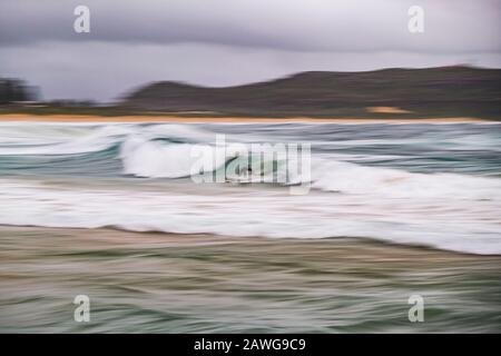 Palm Beach, NSW, Australia. 9th Feb, 2020. A surfer rides a wave in rough conditions (Long exposure). A coastal trough off the NSW coast is being monitored for East Coast Low development over the next 24 hours. This system will move only slowly southwards and bring increasingly widespread and prolonged periods of rain to the hunter and southern NSW coast. High tides forecast on Sunday through to Tuesday may exacerbate flood conditions in low lying coastal areas. A Severe Weather Warning has been issued for the Metropolitan, Illawarra, South Coast and parts of Northern Rivers, Mid North Coast, Stock Photo