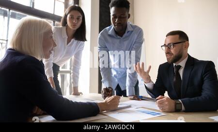 Young and older leaders consider business ideas collaborating at meeting Stock Photo