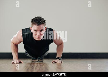 Determined strong young man doing push-ups and looking at camera Stock Photo