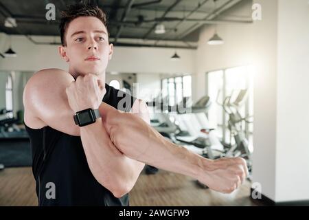 Determined strong young man doing stretching exercise for his arms Stock Photo