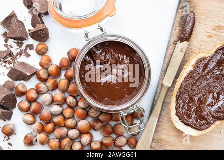 Homemade vegan hazelnut chocolate spread on sourdough bread and in a kilner jar, with unshelled hazelnuts and chunks of dark chocolate Stock Photo