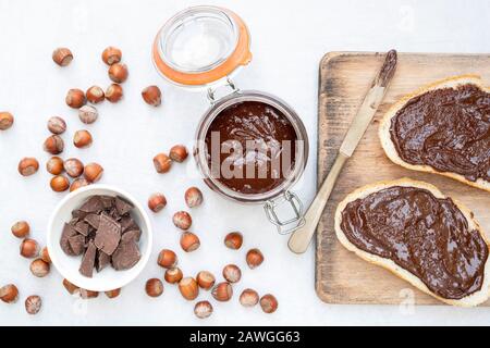 Homemade vegan hazelnut chocolate spread on sourdough bread and in a kilner jar, with unshelled hazelnuts and chunks of dark chocolate Stock Photo